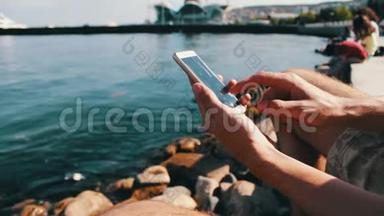 一个年轻人的手在里海的海浪背景下，在智能手机上键入一些东西
